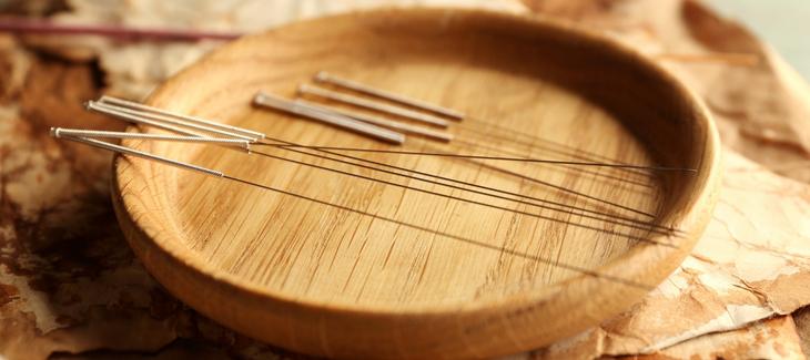 Dřevěná mistička a na ní položení jehly na akupunkturu. 