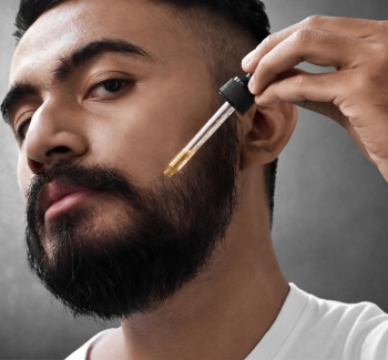Muž aplikující si pečující sérum do vousů. 