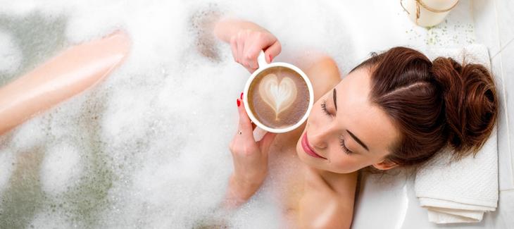 Žena relaxující ve vaně v šálkem kávy v rukou. 
