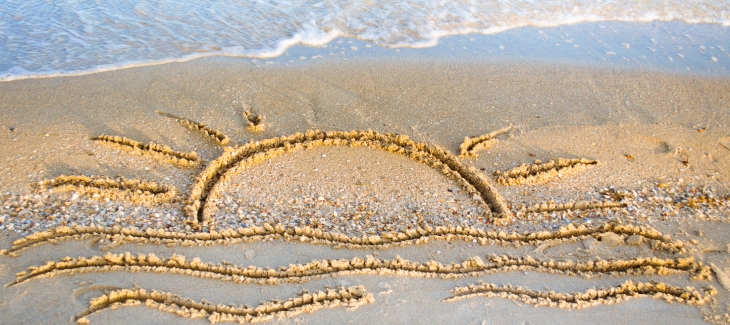 Slunce a moře nakreslené v písku. 