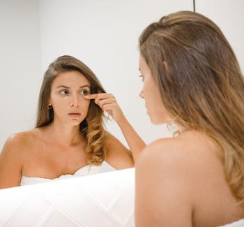 Žena prohlížející si v zrcadle vrásky nebo otoky pod očima. 