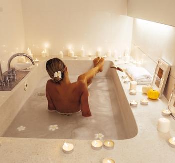 Žena relaxující ve vaně. Podél vany jsou zapálené svíčky. 