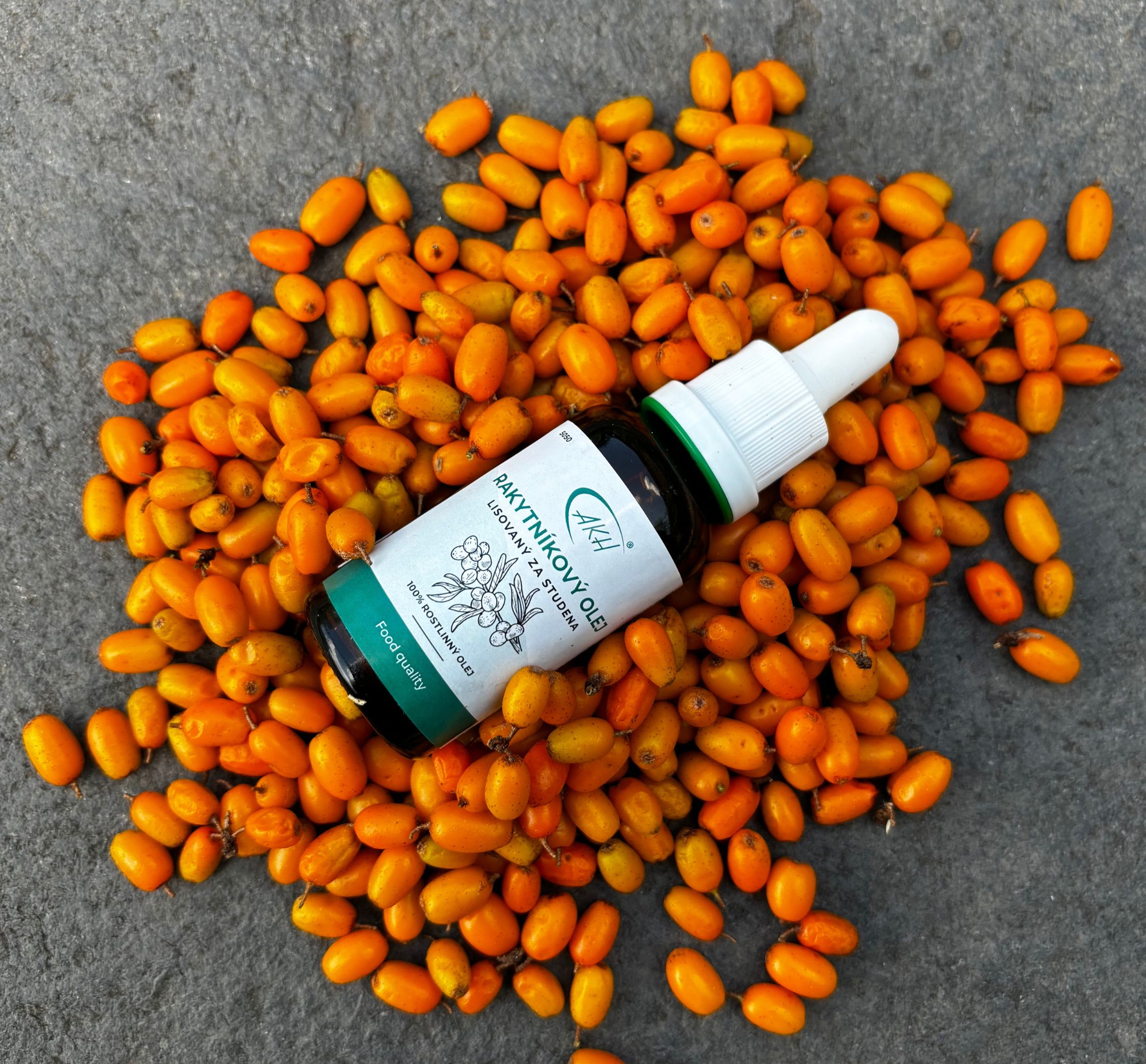 Rakytníkový olej v lahvičce s kapátkem, okolo lahvičky leží plody rakytníku