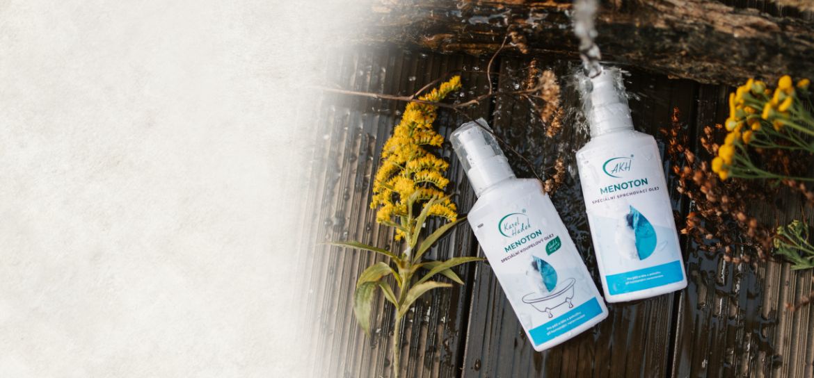 Sprchovací olej MENOTON ležící nad dřevěné podlaze vedle žlutých květin.